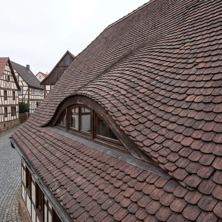 Fledermausgaube: Das Dach schwingt in einer durchgehenden Welle ohne Kante aus der Dachfläche heraus, Biberschwanzziegel folgen der Kurve